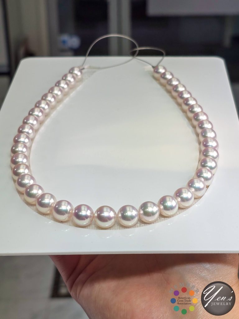 The Tennyo Akoya strand laid on a white tray held in a hand, showing size and luster in daylight