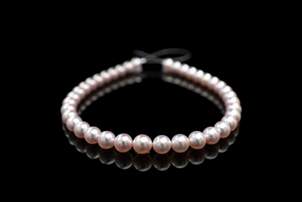 The 10.5 to 11.3 mm Tennyo Akoya strand curved on a black mirror surface, pearls reflecting pink and silver