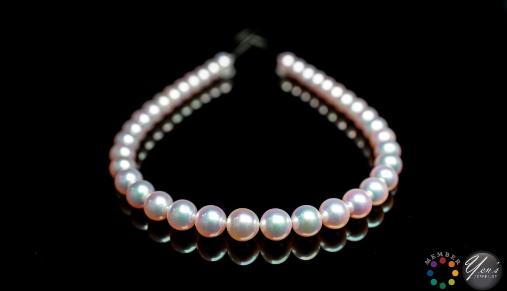 The full Tennyo Akoya strand on a black reflective surface, front pearls showing pink and green overtones