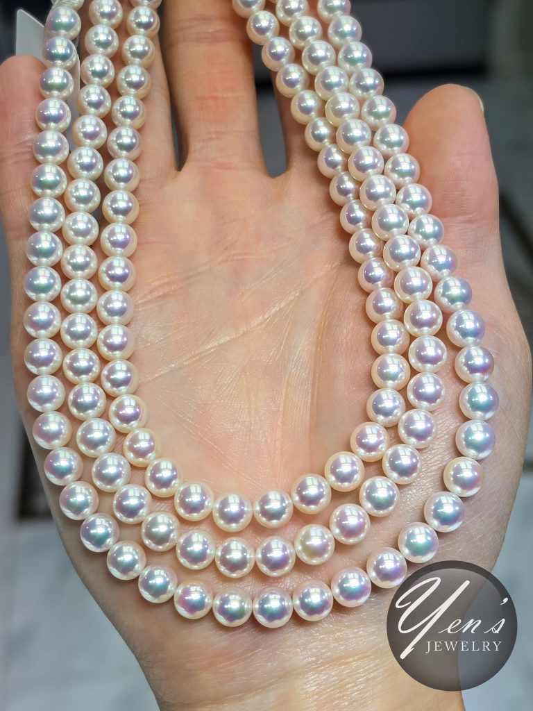 Three 7 to 7.5 mm Tennyo Akoya strands draped over an open hand, each pearl showing pink and green