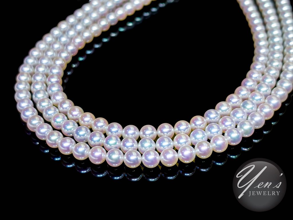 Three strands of 7 to 7.5 mm Aurora Tennyo Akoya pearls on a black mirror surface, pearls showing pink and green overtones